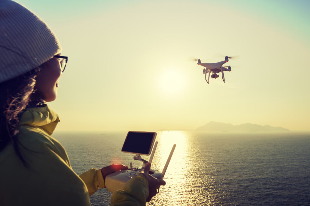 A woman is flying a drone over the ocean, exploring how to make money with the drone.