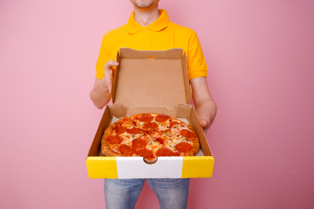 Photo of courier man with pizza box in hands against background of pink wall. make extra cash in the uk delivering pizza.
