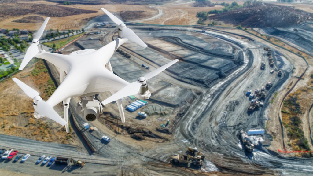 A white drone is flying over a construction site.