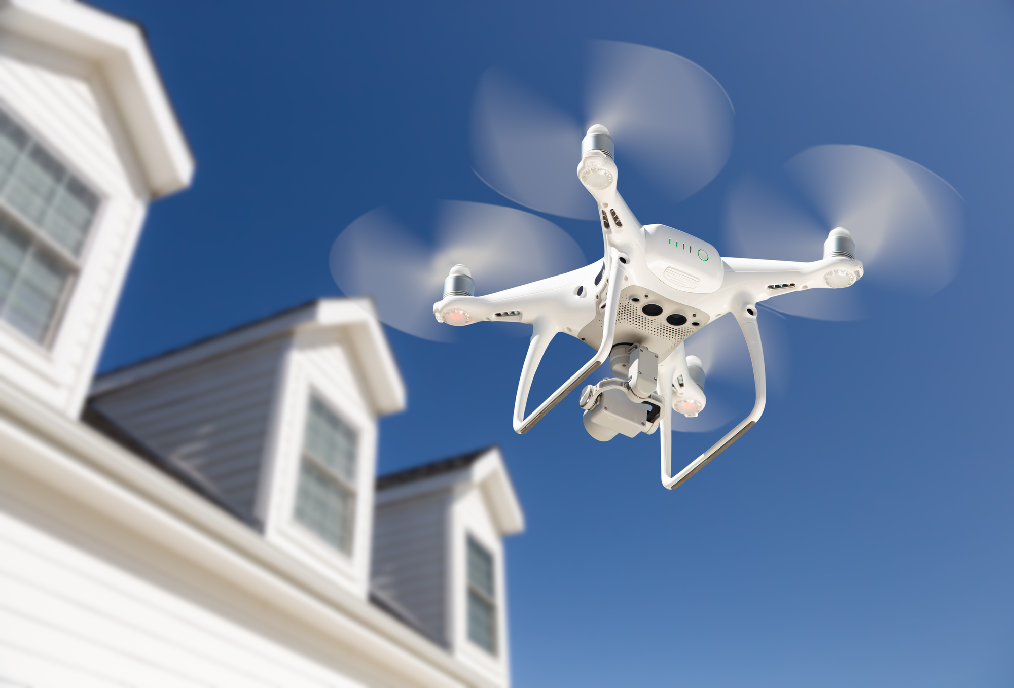 A white drone flying in front of a house.
