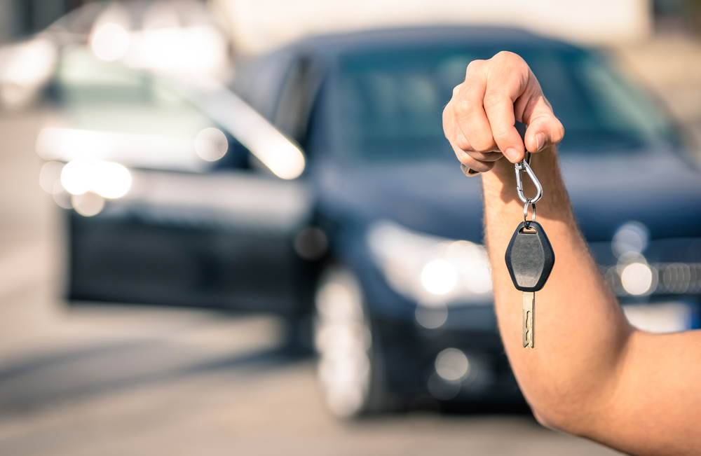 Man's hand holding modern car keys with car out of focus in backgrounf