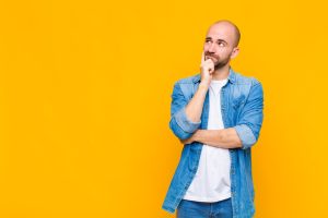 Bald man with a concentrated look, wondering with a doubtful expression, looking up and to the side, against plain bright yellow background. Wondering is matched betting worth it?