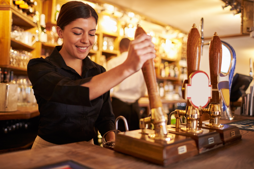 A young woman working behind a bar pulling pints. Make extra money around your day job with some shifts in a pub.