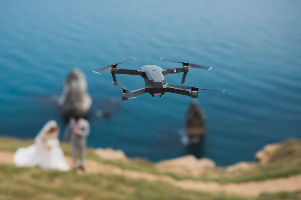 A drone is flying over a bride and groom on a hill.