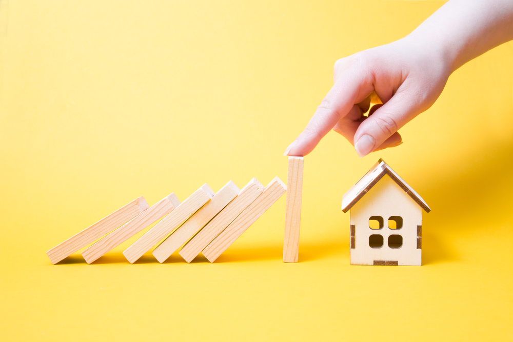 hand stops falling wooden dominoes Falling On House Model, yellow background,