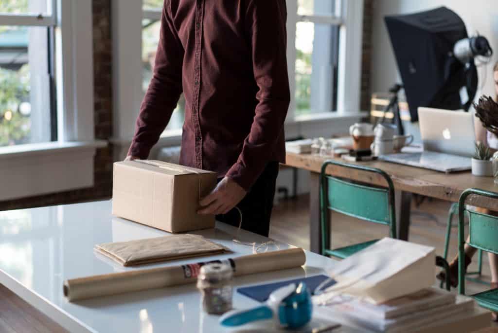 A man packing up a package for Amazon. Selling products on Amazon with FBA can be an easy and lucrative side hustle