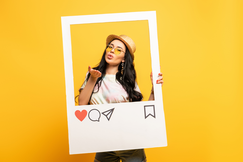 A young woman showcasing her side hustle as social media manager standing in a large Instagram style frame against a vibrant yellow background.