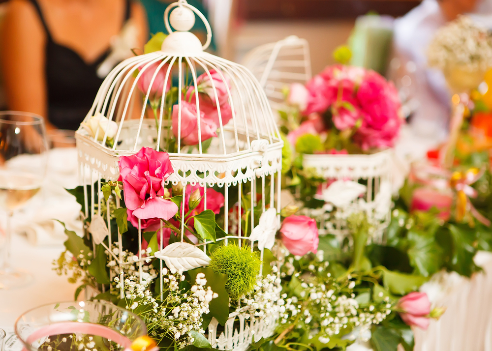 A close up view of the floral wedding decorations, pink and green flowers inside a white birdcage. Renting out your wedding decorations is an idea to make extra money in the UK.