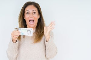 Middle age woman holding 5 pounds bank note over isolated background very happy and excited to get free £5 with zilch referral offer