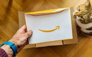 a man's hand holding an Amazon envelope with a cat watching