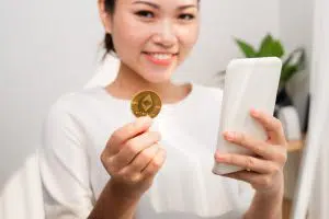 woman holding up an Ethereum crypto coin and a smart phone