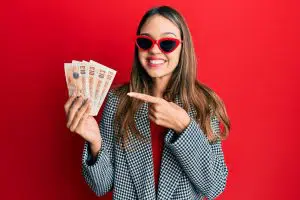 a young brunette woman holds a wad of UK £10 bank notes