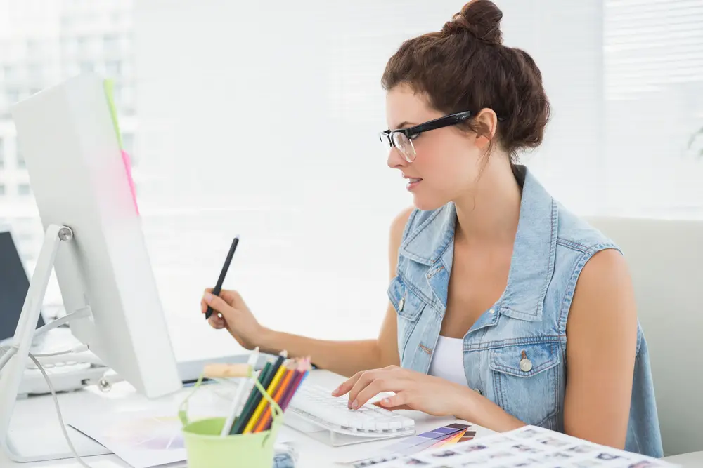 a freelance graphic designer at her desk with compuet and pot of colourful pencils
