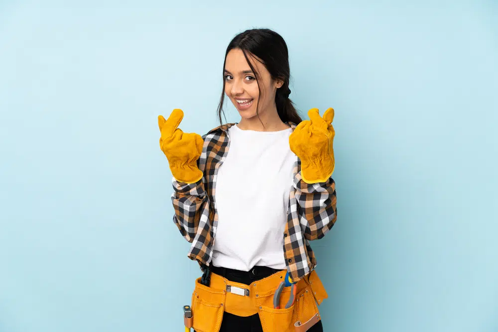 Young electrician woman isolated on blue background making money gesture