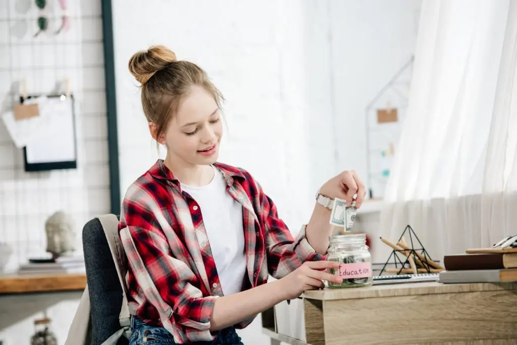 a teen girl putting her savings in a jar