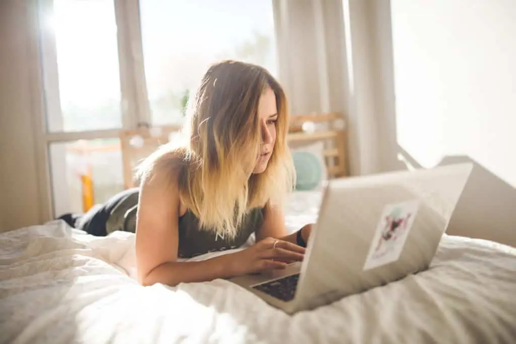 girl on laptop on bed. doing surveys online with Prolific Academic is a good way to make money from home.