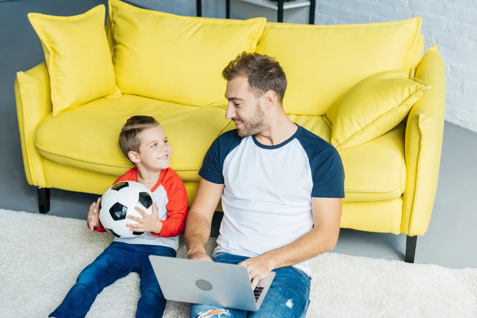 a dad working online with laptop and son with football