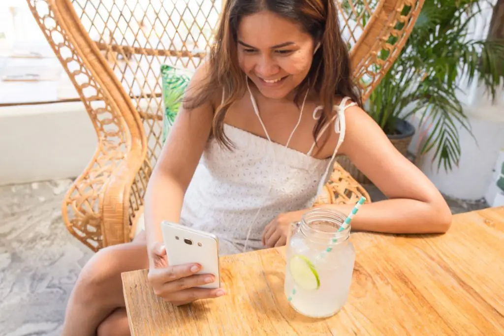 smiling girl looking at her phone with a drink