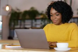 a woman in yellow jumper works at her laptop as freelance proofreader
