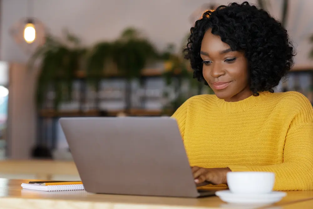 a woman in yellow jumper works at her laptop as freelance proofreader