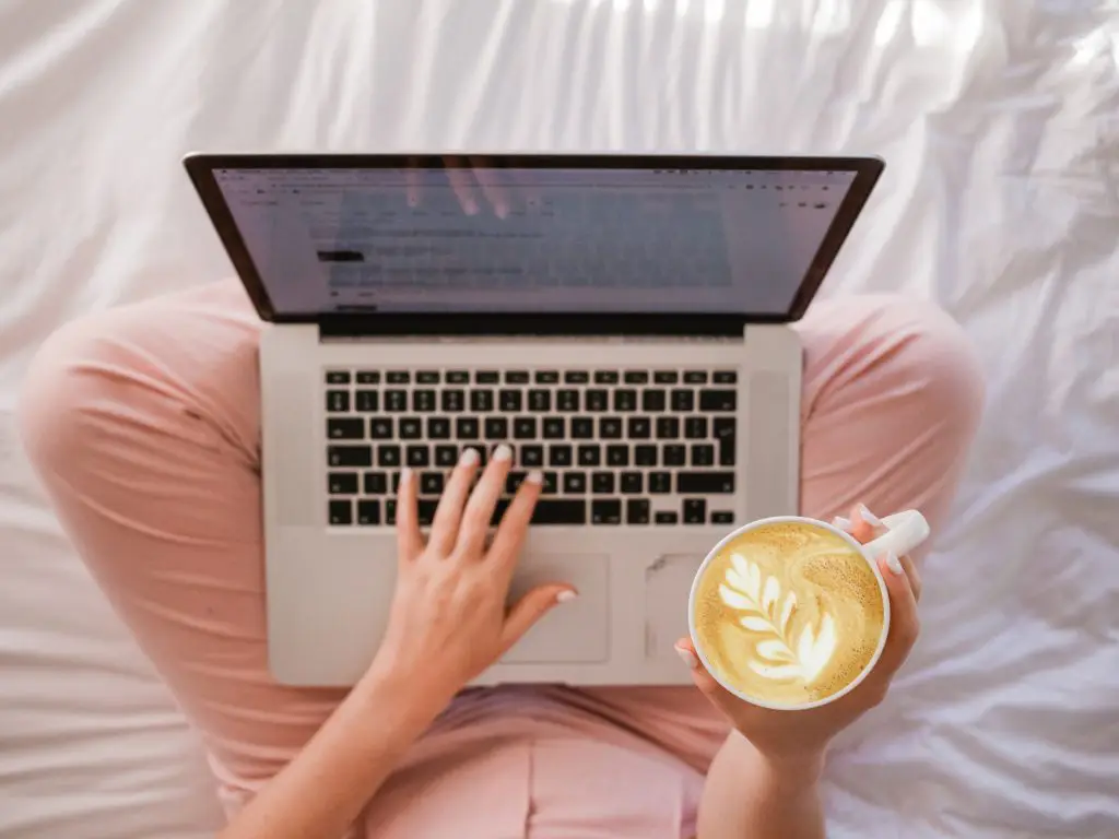 woman working from laptop in bed with coffee