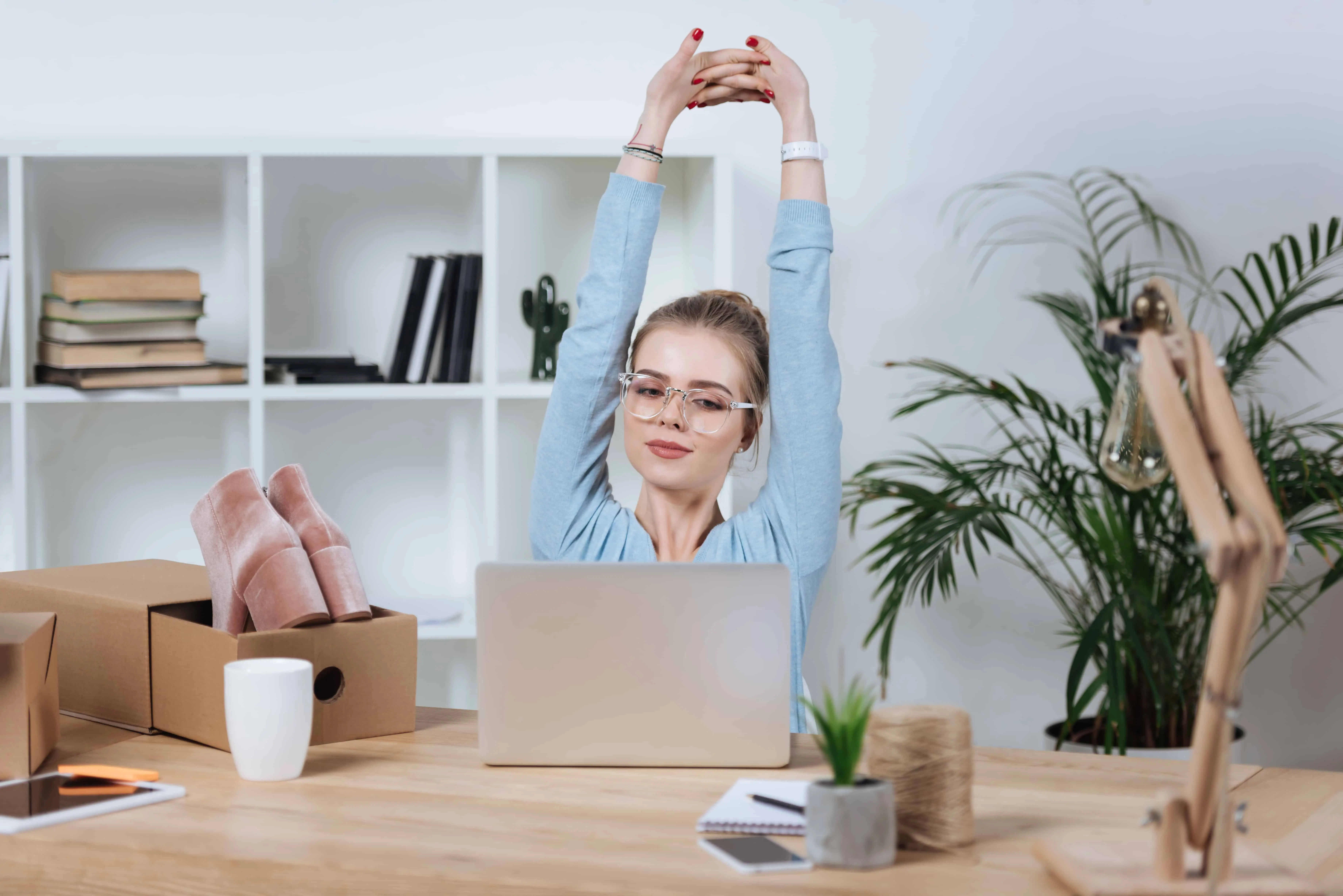 work from home jobs for mums - a woman stretching at her computer with a box of shoes ready to ship and sell online